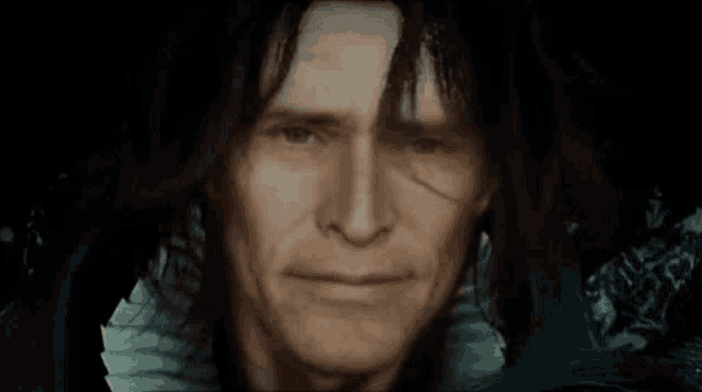 a man with long black hair looks at the camera