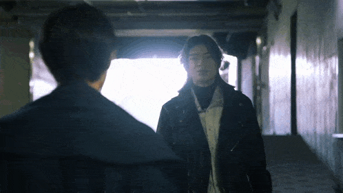two men are standing next to each other in a dark hallway .