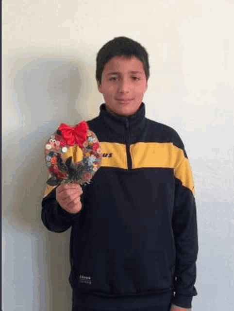 a young boy in a yellow and black jacket is holding a handmade christmas wreath .