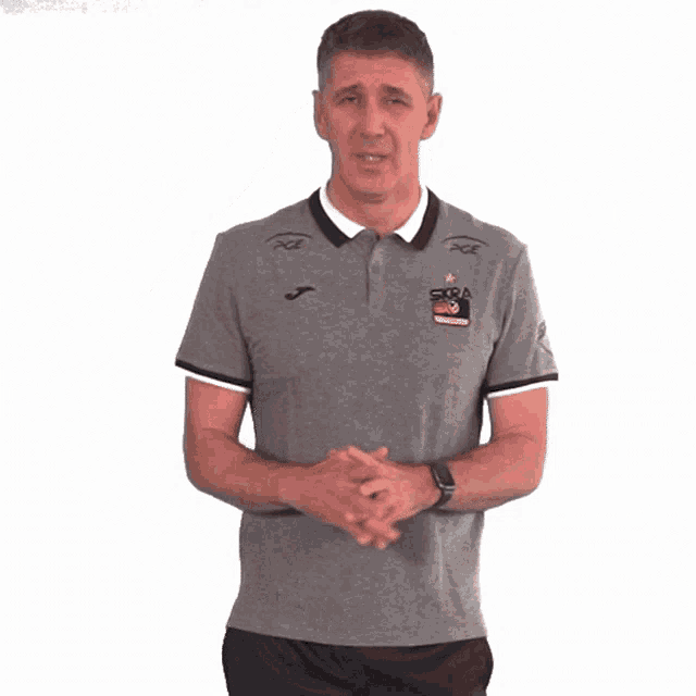 a man wearing a grey shirt that says sfera on it holds his hands to his head
