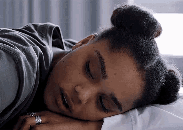 a woman is sleeping in a bed with her eyes closed and her hand on her head .