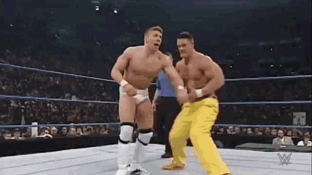 two men are wrestling in a wrestling ring and one of them is laying on the ground .