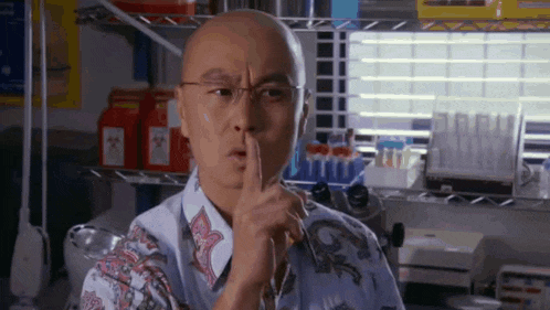a bald man wearing glasses is holding his finger to his lips .