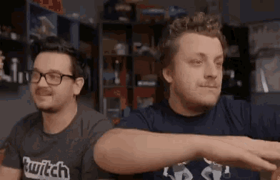 two men are sitting next to each other in a room and one of them is wearing a shirt that says twitch on it .