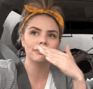 a woman wearing a yellow headband and a gray sweater is covering her mouth with her hand .