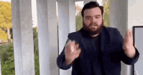 a man with a beard is standing in front of a white railing making a funny face .