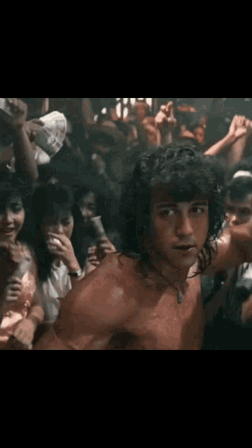 a shirtless man with long curly hair is standing in a crowd of people .
