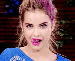 a woman with pink hair is sticking out her tongue and wearing a blue shirt