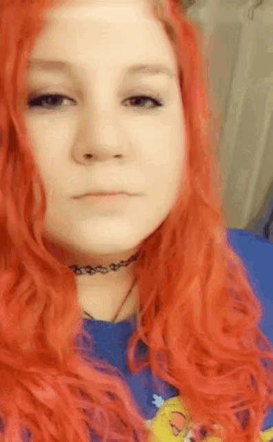 a woman with red hair wearing a choker and a blue shirt