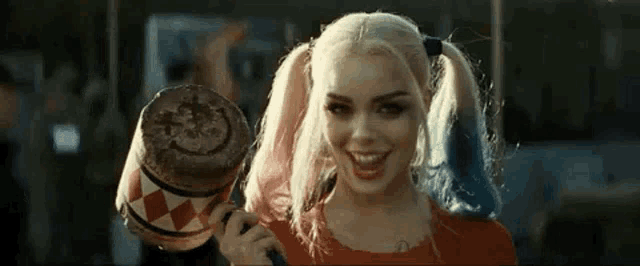 a woman in a harley quinn costume is smiling and holding a mallet .