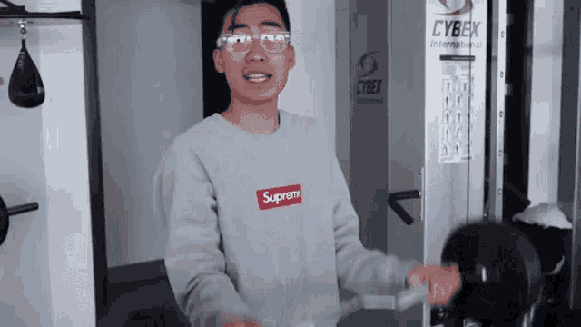 a man wearing a supreme sweatshirt is lifting weights