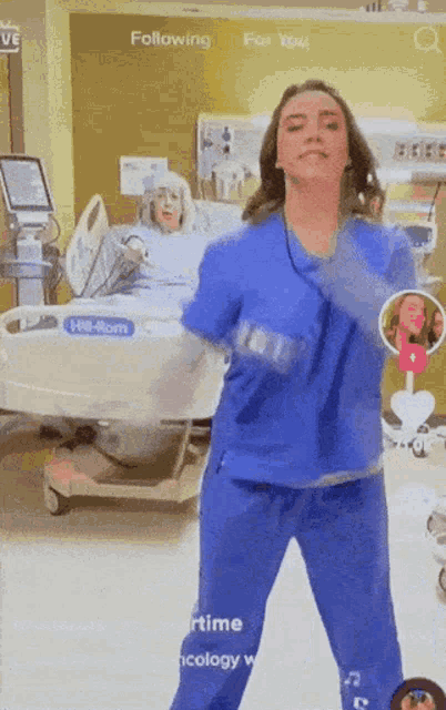 a woman in blue scrubs is dancing in front of a hospital bed that says hill rom
