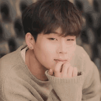 a close up of a young man wearing a sweater and earrings with his hand on his chin .