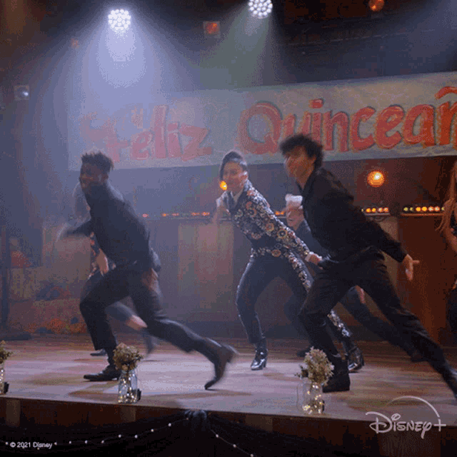 a group of people are dancing in front of a sign that says " feliz quincean "