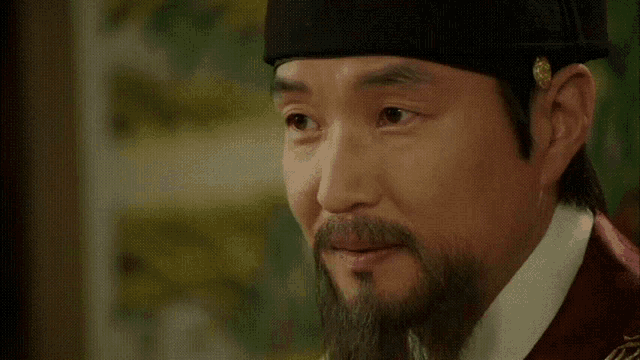 a close up of a man with a beard wearing a hat and looking at the camera .