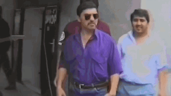 a man wearing sunglasses and a purple shirt is walking with other men