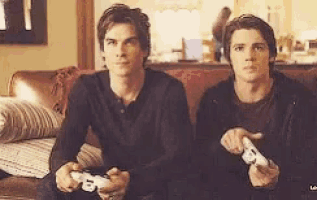 two young men are sitting on a couch playing a video game with controllers .