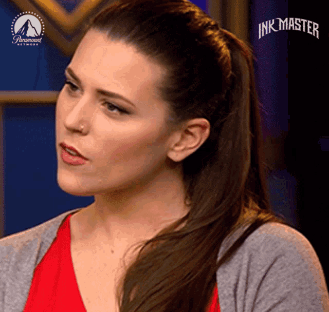 a woman with a ponytail and a gray sweater is on a show called ink master