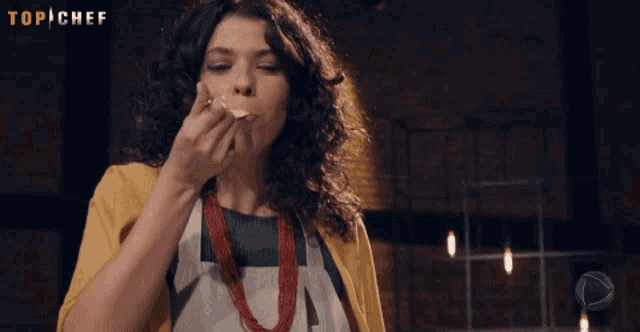 a woman is eating a piece of food with a top chef logo in the background