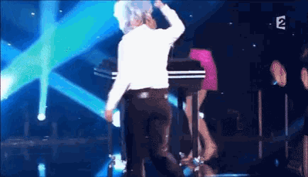 a man in a white shirt is dancing on a stage in front of a sign that says ' 2 '
