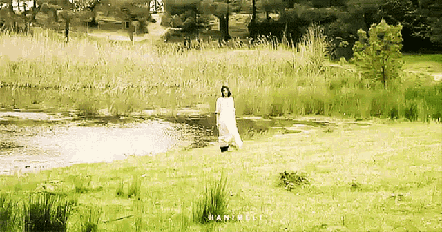 a woman in a white dress is standing in the grass near a lake
