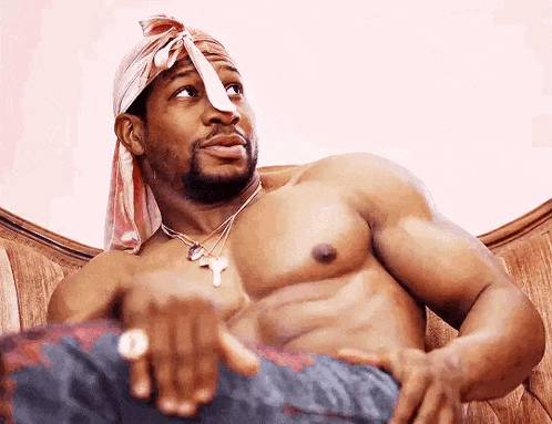 a shirtless man is sitting on a couch wearing a bandana and a ring .