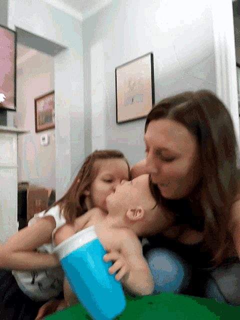 a woman kisses a baby on the cheek while another girl holds a blue cup