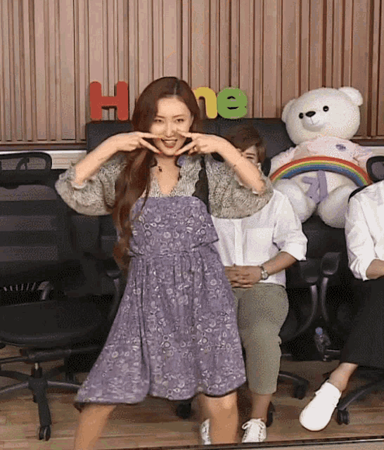 a woman in a purple dress is making a funny face in front of a teddy bear with the word home on it