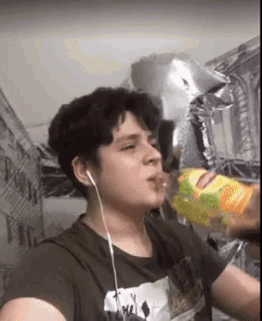 a young man is drinking from a bottle while wearing headphones and holding a balloon .
