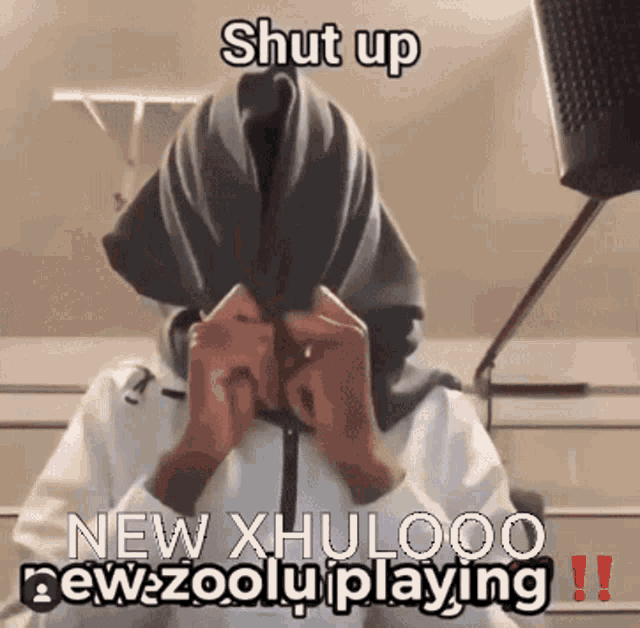 a person covering their face with a scarf with the words shut up new xhulooo new zoolu playing