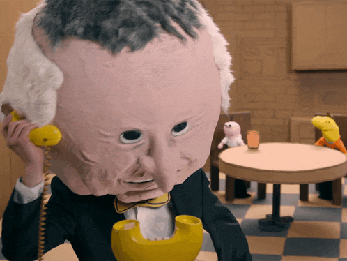 a puppet with a big head is talking on a yellow telephone