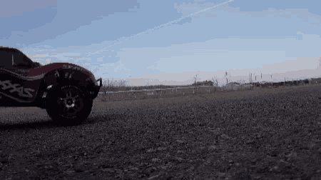 a red rc car is driving on a dirt road .