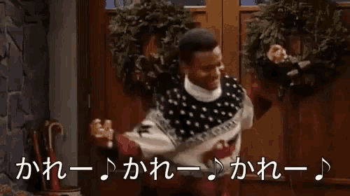 a man in a sweater is dancing in front of a door with a wreath in the background .