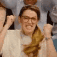 a woman wearing glasses is making a funny face while raising her fist in the air .