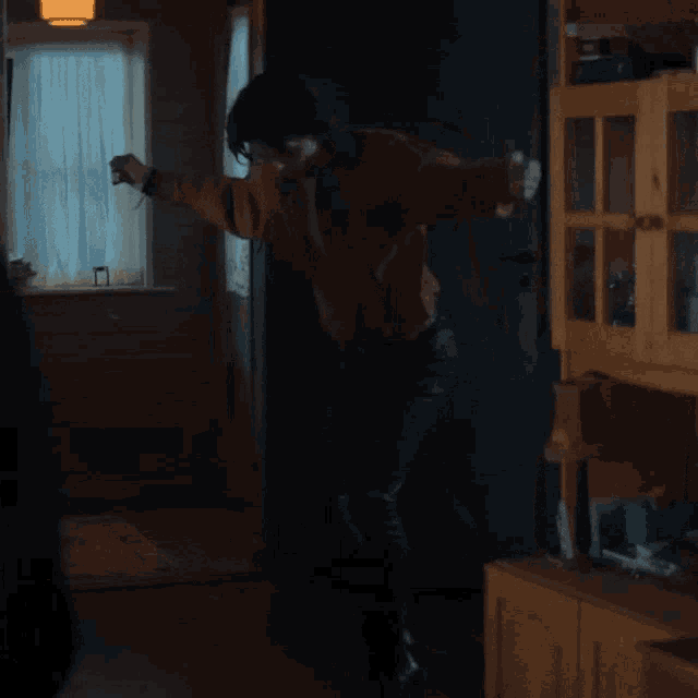 a man in a brown shirt is standing in a dark room with his arms outstretched