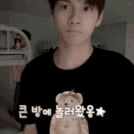 a young man wearing a black t-shirt with a teddy bear on it is standing in a room .
