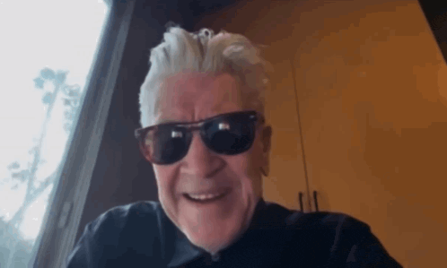 an older man wearing sunglasses and a black shirt is smiling