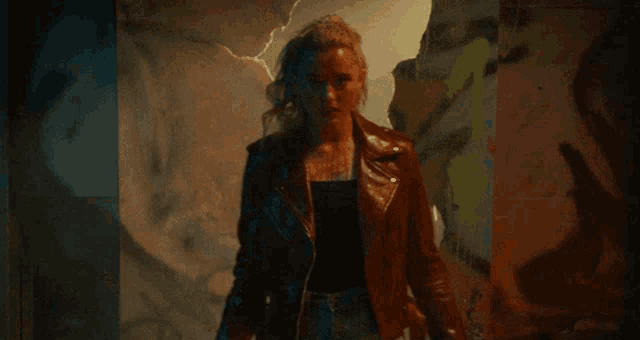 a woman in a leather jacket stands in a dark room