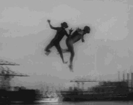 a black and white photo of two people jumping into the water .