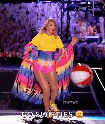 a woman in a colorful dress is holding a beach ball on stage .