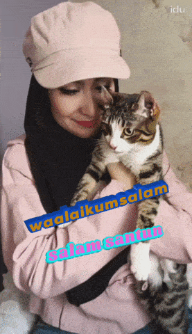 a woman in a pink hat holds a cat in her arms with the words waalaikumsalam written on the bottom