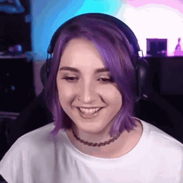 a woman with purple hair wearing headphones and a choker is smiling .