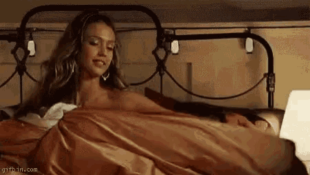 a naked woman is laying in bed with a laptop on her lap .