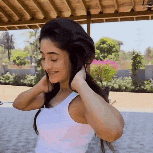 a woman in a white tank top holds her hair