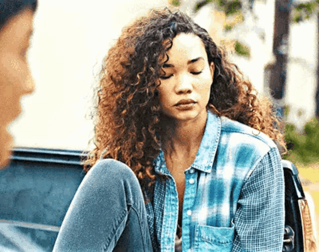 a woman with curly hair is sitting in the back of a car with her legs crossed .