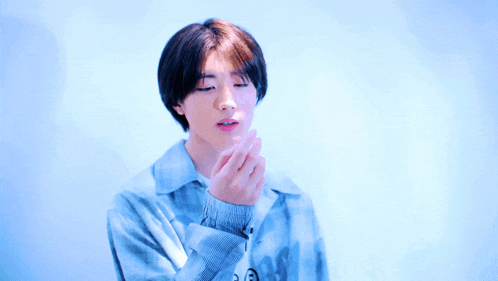 a young man in a blue plaid shirt is making a heart shape with his hand