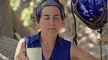 a woman in a blue shirt is holding a cup of coffee and making a funny face .