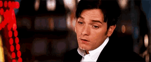 a man in a tuxedo and bow tie is sitting in front of a christmas tree .