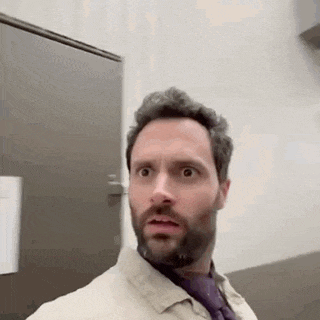 a man with a beard and tie is standing in front of a door and making a funny face .