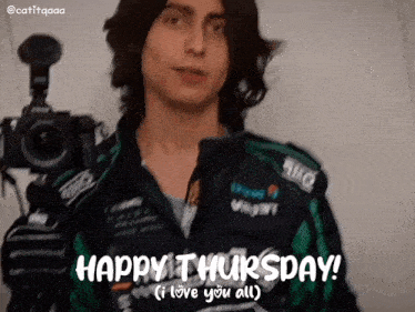 a man in a green jacket is holding a camera and saying happy thursday